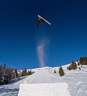 Snowboarder springt im Absolut Park, Snow Space Salzburg, umgeben von schneebedeckten Bergen.