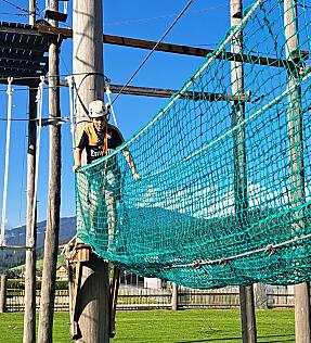 Kind balanciert sicher durch das grüne Netz des Hochseilgartens in Flachau.