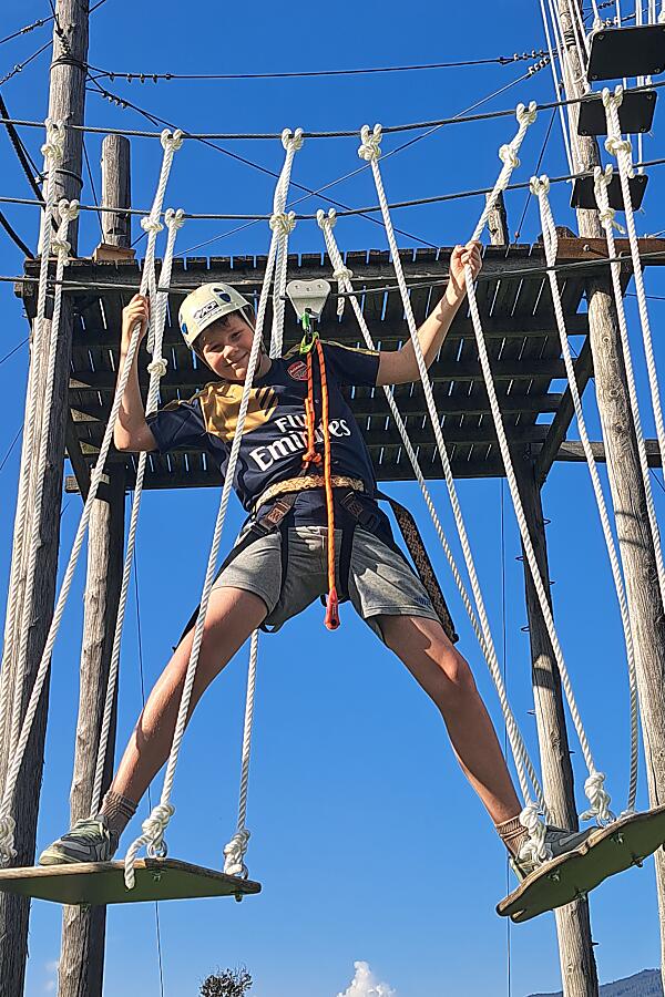 Boy conquering a climbing challenge at the kids high ropes course in Flachau under a bright blue sky.