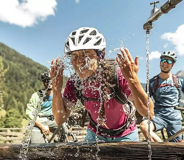 Woman cooling off at a mountain spring during an e-bike tour in Flachau, summer holiday in the Austrian Alps