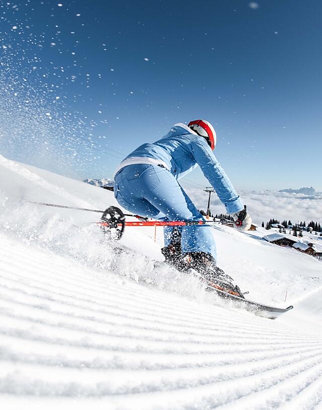 Skier in blue outfit carving down a freshly groomed slope in Flachau under a clear blue sky, winter holiday in the Austrian Alps