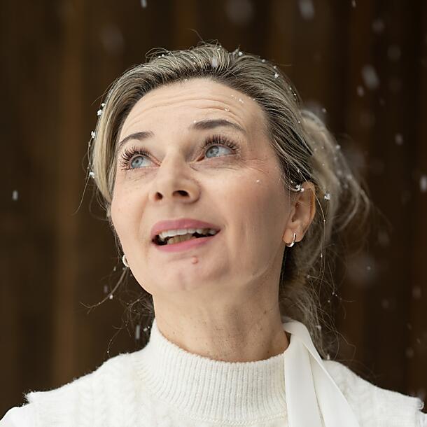 Kim – Rezeptionistin & Wellnessexpertin mit Herz | almlust Flachau Kim, Rezeptionistin und ausgebildete Physiotherapeutin im Hotel almlust, blickt lächelnd in den winterlichen Schneefall.