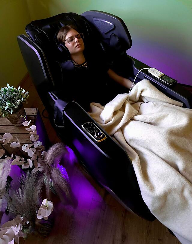 Frau entspannt im Brainlight Massagesessel mit Kopfhörern und Decke im Wellnessbereich der Almlust