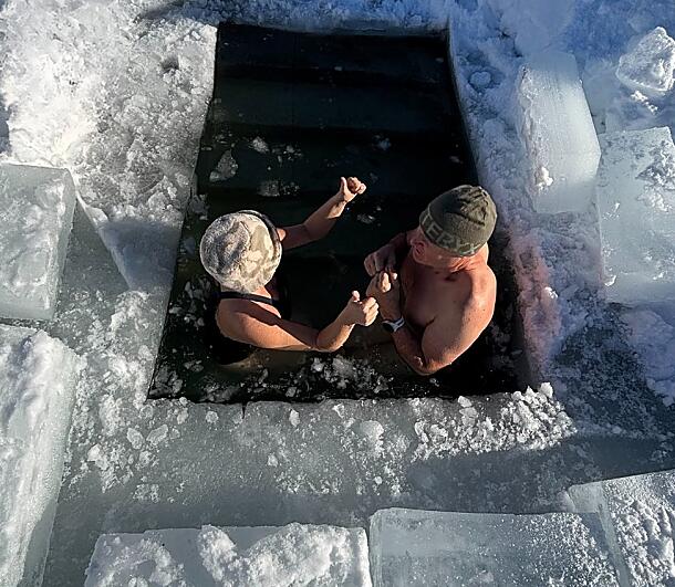 wo people ice bathing in a frozen lake hole during a winter retreat
