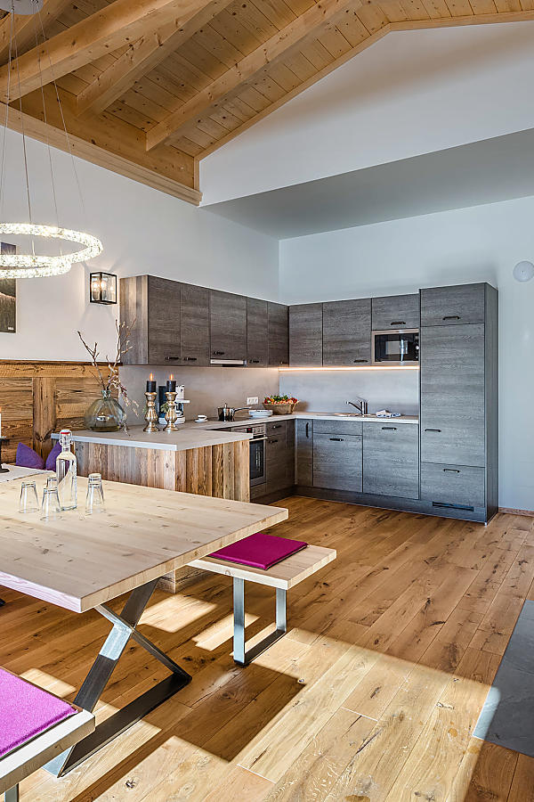 Apartment kitchen with dining table, wooden bench, grey cabinets, and a lit fireplace.