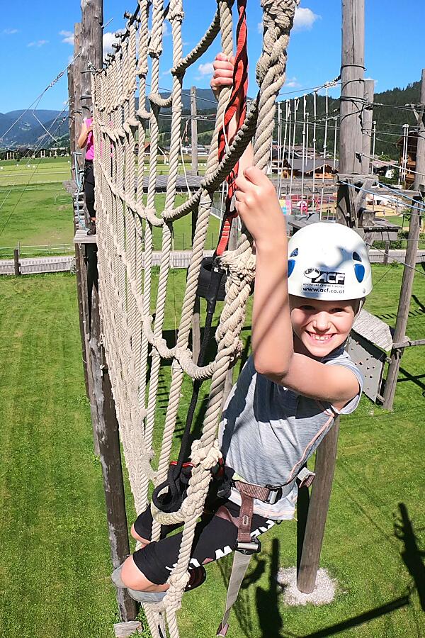 Smiling child climbing a rope bridge at the high ropes course in Flachau