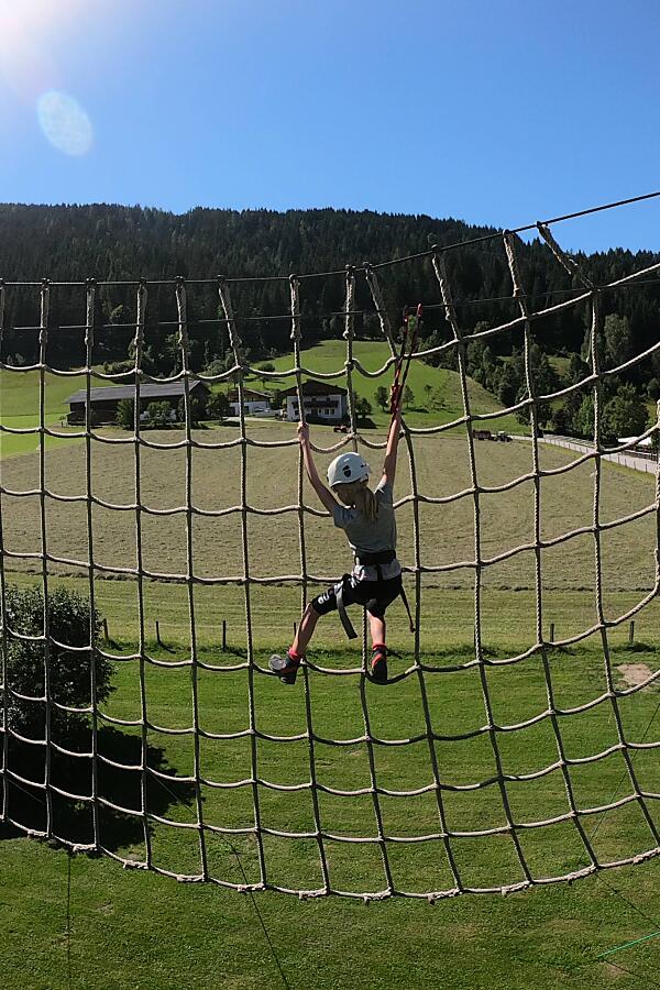 Child climbing the large rope net at the high ropes course in Flachau