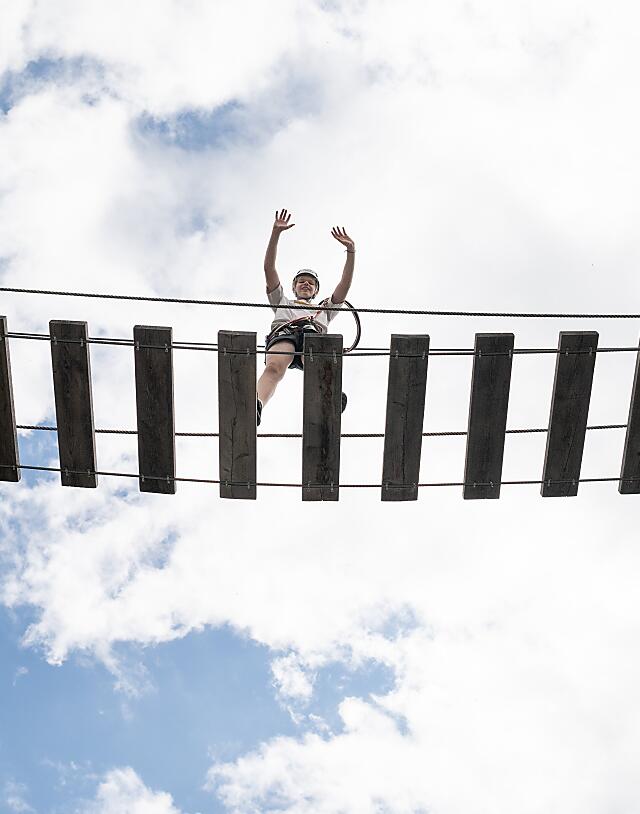 Child crossing the hanging bridge hands-free on the almlustrock climbing tower in Flachau