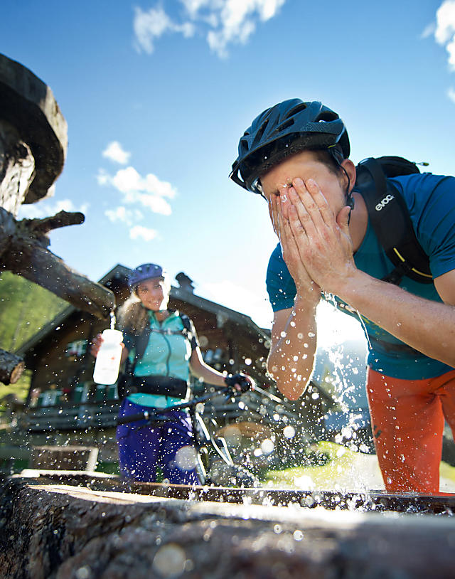 Mountain biker cooling off at alpine fountain – refreshing summer ride in Flachau