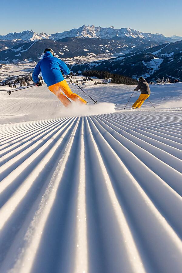 Skifahrer auf einer sonnigen Piste im Snow Space Salzburg bei Flachau mit Seilbahn und Tal im Hintergrund