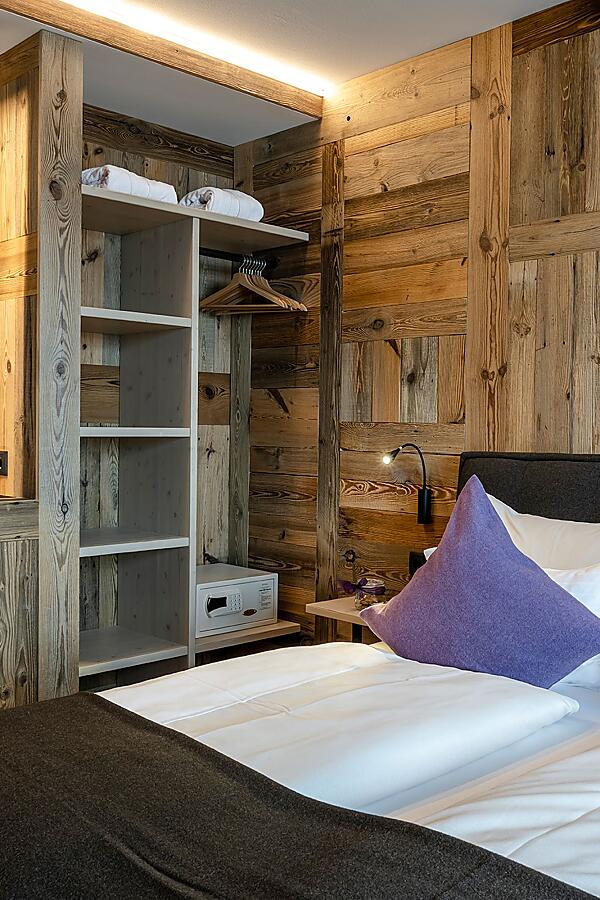Gemütliches Doppelzimmer in der almlust mit Holzwand, offenem Schrank und lila Kissen