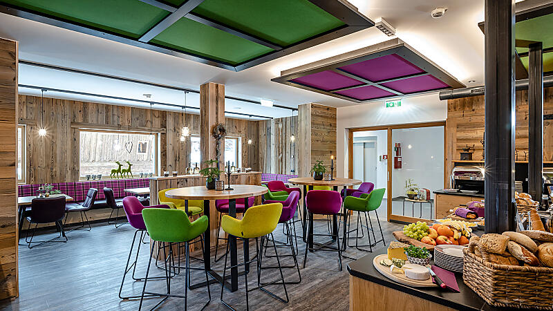 Breakfast area at almlust with colourful chairs, high tables and breakfast buffet