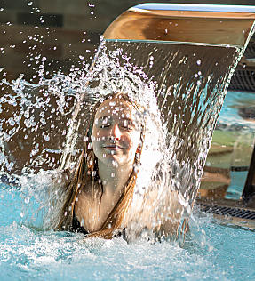 Guest enjoying a neck massage under a waterfall in the indoor pool at almlust in Flachau