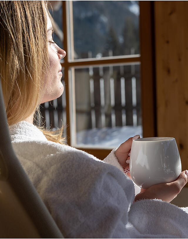 Woman relaxing in a bathrobe in a relaxation room with mountain view at almlust in Flachau