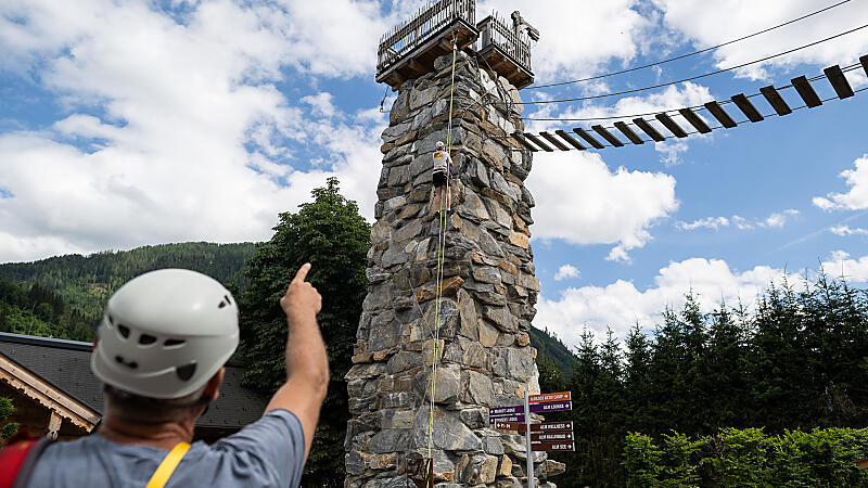 Person mit Helm zeigt auf den almlustrock mit Hängebrücke und Klettersteig in der almlust in Flachau