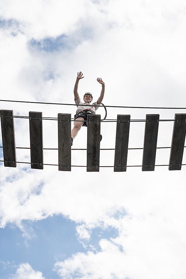 Person steht auf einer Hängebrücke der almlust vor hellem Himmel und erlebt Sport vor Ort in luftiger Höhe