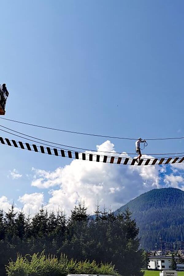 Person balancing on a suspension bridge at almlust with views of almlustrock, mountains and blue sky in Flachau