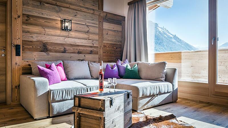 Bright living area at almlust with large sofa, lots of wood, balcony and mountain views
