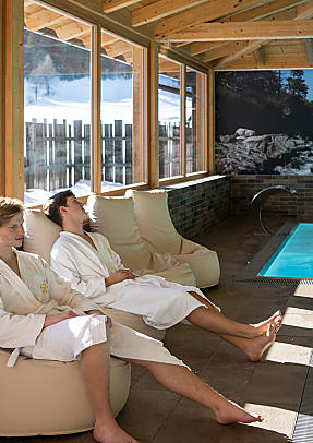 Two guests in bathrobes relaxing by the indoor pool at Almlust